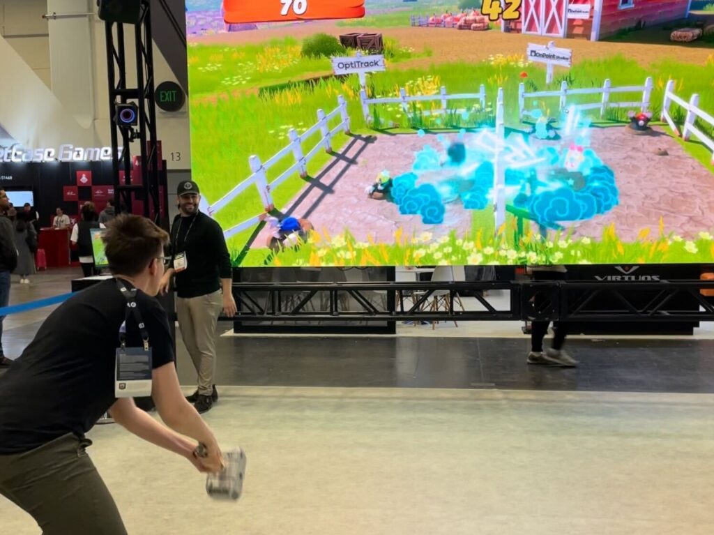 A photo of one person holding a toy hammer standing in front of a projected screen. The person is controlling an in-game object with the toy hammer.