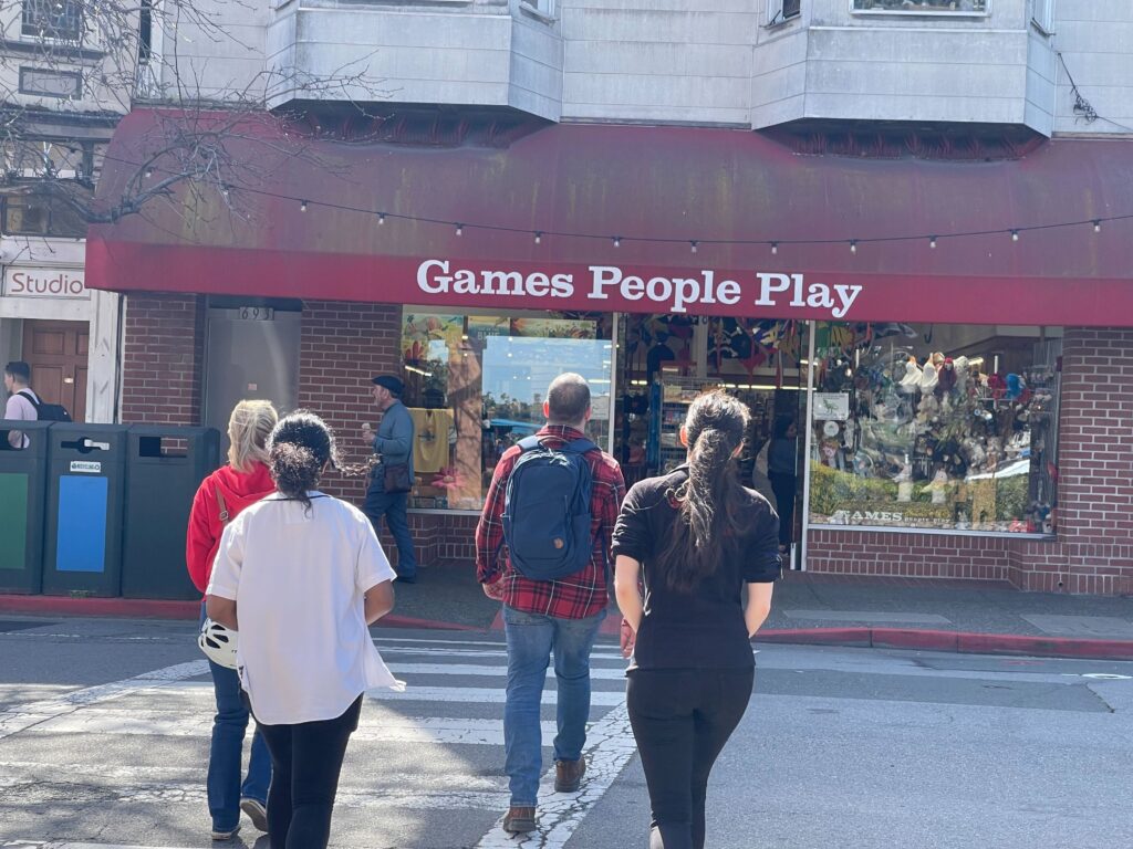 A rear photo of four people walking towards a show with an awning that reads "Games People Play."